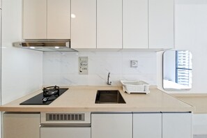 Une cuisine moderne dotée d’une cuisinière à gaz, d’une hotte en acier inoxydable, de meubles blancs, d’un pare-feu en marbre et d’une fenêtre offrant une vue sur les bâtiments.