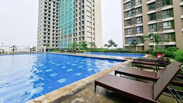 Una piscina con sillones de descanso, rodeada de edificios residenciales altos.