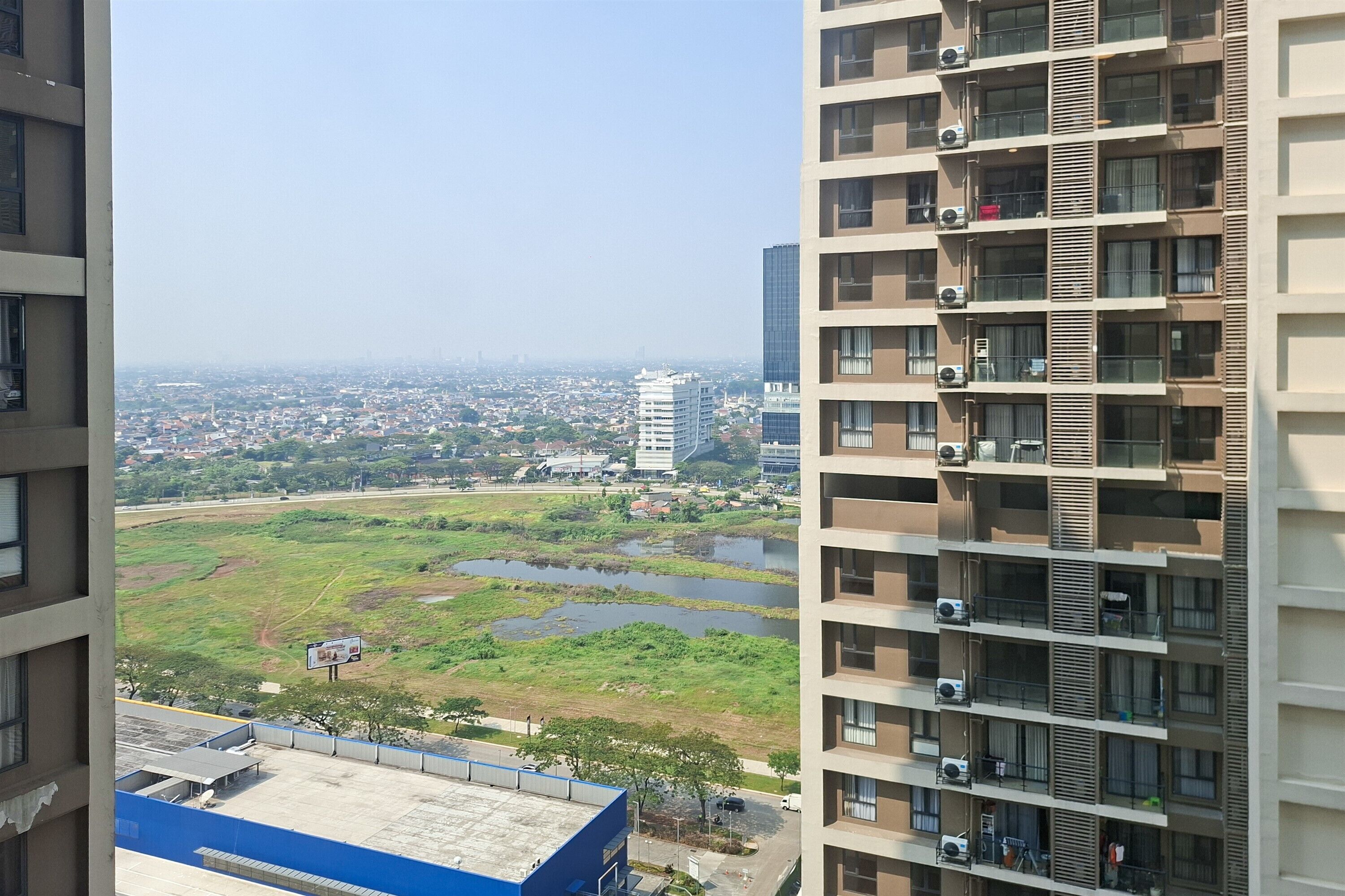 Un immeuble de grande hauteur doté de nombreux balcons, offrant une vue sur le paysage urbain, et une rivière bordée de verdure au premier plan.