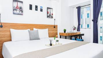 A hotel room with a wooden headboard, a bed with white linens, a bedside table with a plant, and artwork on the wall.