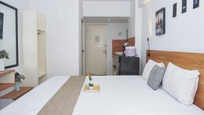 Hotellihuone, jossa on sänky, työpöytä, peili ja ovi, joka johtaa kylpyhuoneeseen.