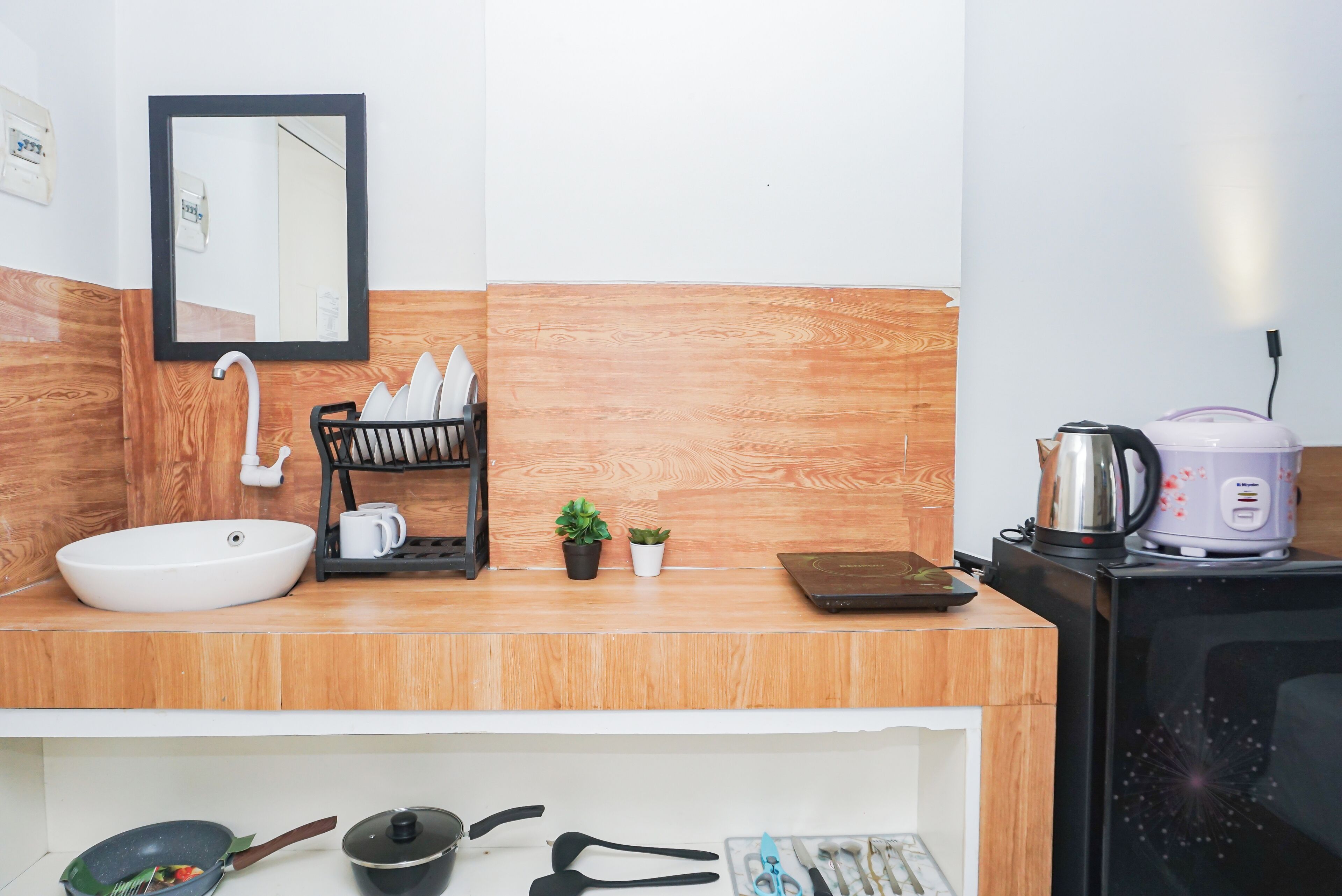 A modern kitchen with a white sink, a black dish rack, a small potted plant, a kettle, and a microwave.