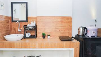 A modern kitchen with a white sink, a black dish rack, a small potted plant, a kettle, and a microwave.