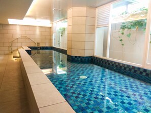 A swimming pool with blue mosaic tiles, a tiled deck, and a window with plants. - Charming Modern Studio At Apartment Mustika Golf Residence (Cikarang)