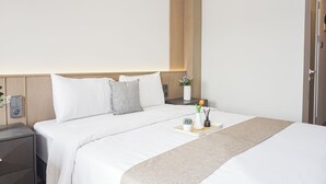 Quarto de hotel com cama, mesas de cabeceira, um vaso com flores e uma bandeja com vela e planta.