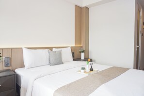 A hotel room with a bed, bedside tables, a nightstand, a vase with flowers, and a tray with a candle and a small plant. - Charming Modern Studio At Apartment Mustika Golf Residence (Cikarang)