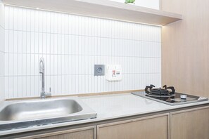 A kitchen with a stainless steel sink, a gas stove, and a white tiled backsplash. - Charming Modern Studio At Apartment Mustika Golf Residence (Cikarang)