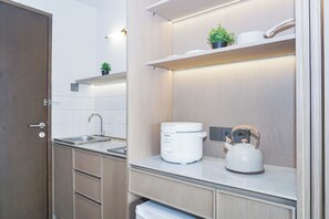 A modern kitchen with a built-in sink, a kettle, and a small potted plant on the countertop. - Charming Modern Studio At Apartment Mustika Golf Residence (Cikarang)