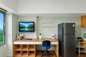Una cocina moderna con refrigerador integrado, un escritorio de madera con una silla, televisor montado y ventana con vista a la ciudad.