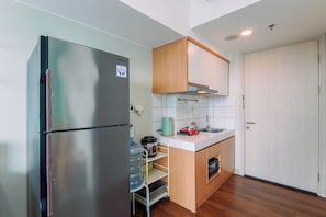 A compact kitchen with a stainless steel refrigerator, wooden cabinets, a built-in oven, and a small sink. - Neat And Nice Studio Room At Apartment Springlake Summarecon Bekasi (Bekasi)
