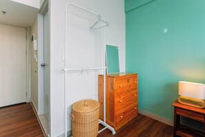 Une pièce comprenant une commode en bois, un portant à vêtements, un panier en osier et une petite table avec une lampe.