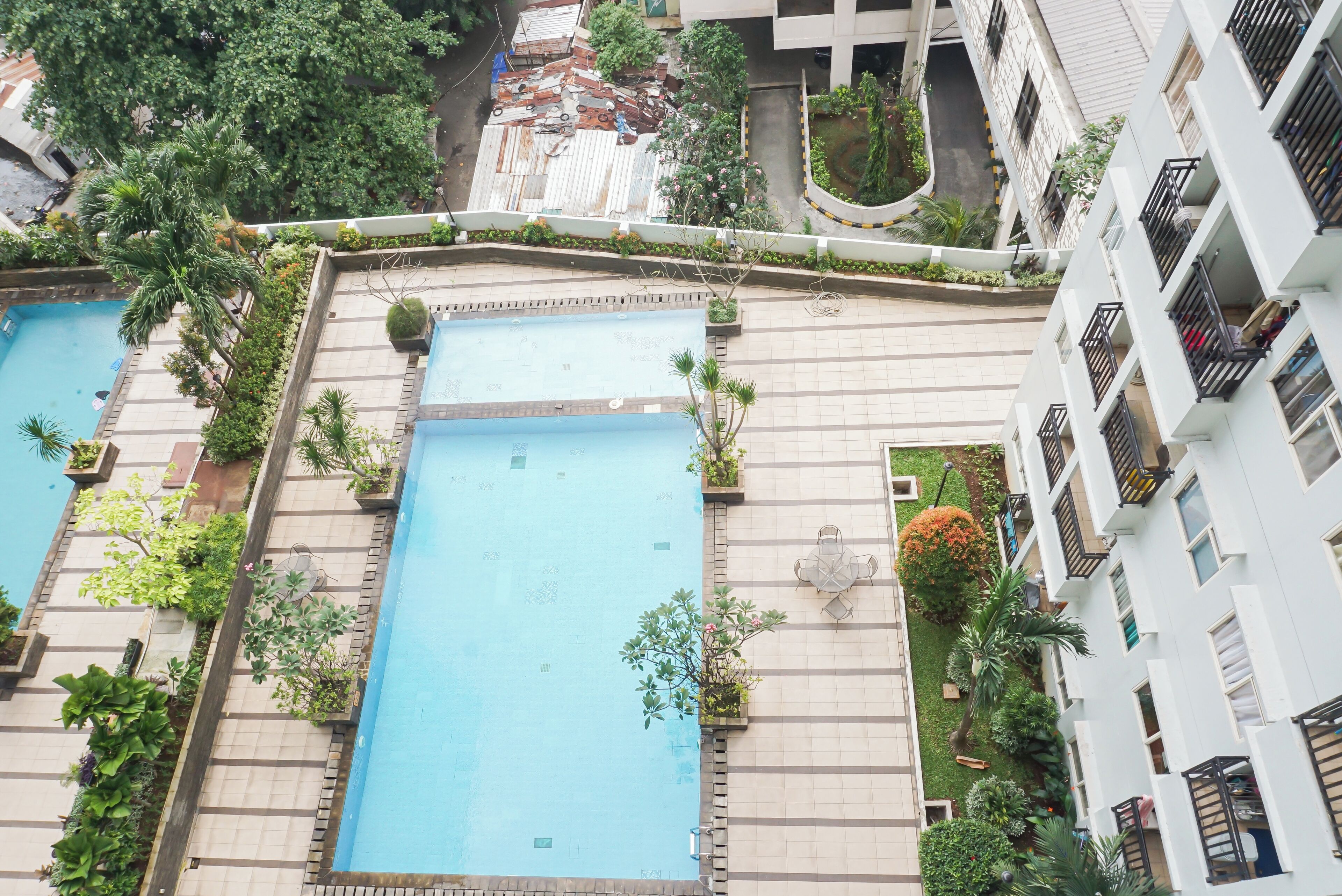A residential building with two swimming pools, surrounded by greenery and a well-maintained garden.