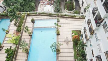 A residential building with two swimming pools, surrounded by greenery and a well-maintained garden.