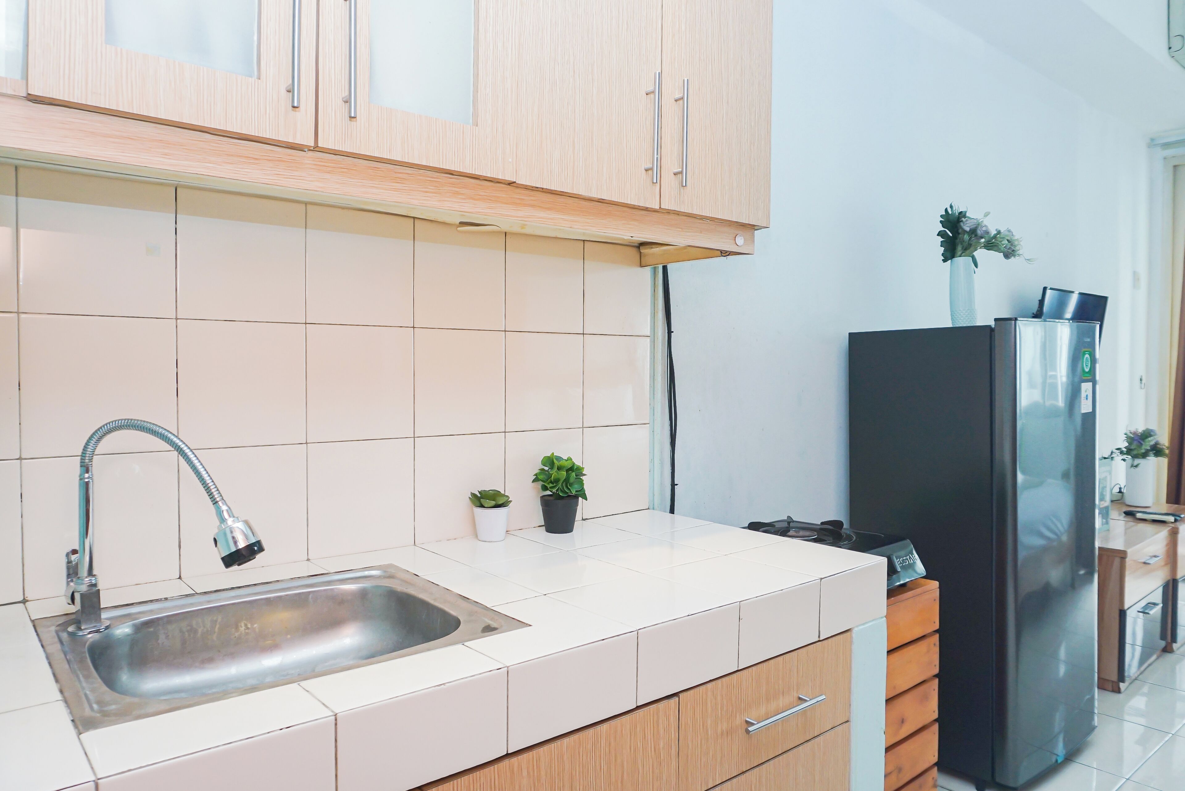 Eine moderne Küche mit Spüle aus Edelstahl, Holzschränken, einem schwarzen Kühlschrank und einem kleinen Topfpflanzen.