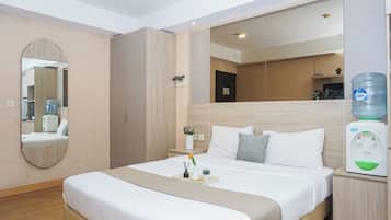 A hotel room with a large bed, a bedside table, a water dispenser, a mirror, and a view of the hallway.
