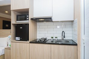 A compact kitchen with a microwave, a gas stove, and a sink. - Cozy Stay Studio At Apartment Metropark Condominium Jababeka (Cikarang)