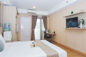 A hotel room with a bed, a desk, a TV, a water dispenser, and a window with curtains. - Cozy Stay Studio At Apartment Metropark Condominium Jababeka (Cikarang)