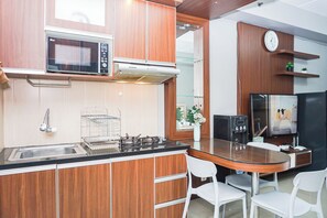 A modern kitchen with wooden cabinets, a microwave, gas stove, and a refrigerator. - Good Warm Studio Room At Apartment Metropark Condominium Jababeka (Cikarang)