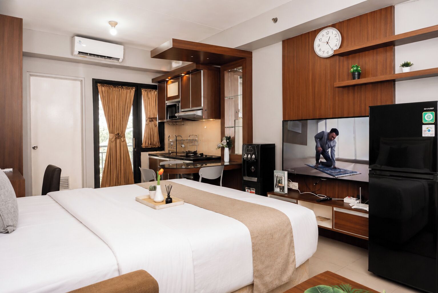 Ein Hotelzimmer mit einem Bett, einem Schreibtisch mit Computer, einem Fernseher und einer Küchenzeile.