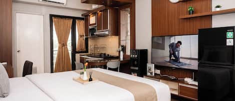 Quarto de hotel com uma cama, escrivaninha com computador, televisão e cozinha compacta.