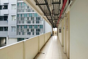 A corridor with a tiled floor, a metal railing on one side, and a view of a building with multiple windows and air conditioning units. - Good Homey 2Br At Apartment Menteng Square (Jakarta)