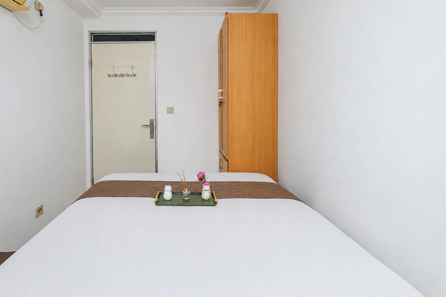 Une chambre d’hôtel avec un lit, une armoire en bois, une porte avec une poignée et une petite table agrémentée d’objets décoratifs.