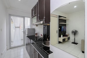 A modern kitchen with a gas stove, a refrigerator, and a microwave. There is a dining area with a table and chairs. - Good Homey 2Br At Apartment Menteng Square (Jakarta)
