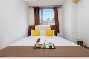 A hotel room with a bed, a window with curtains, a tray with items, and a wall clock. - Good Homey 2Br At Apartment Menteng Square (Jakarta)