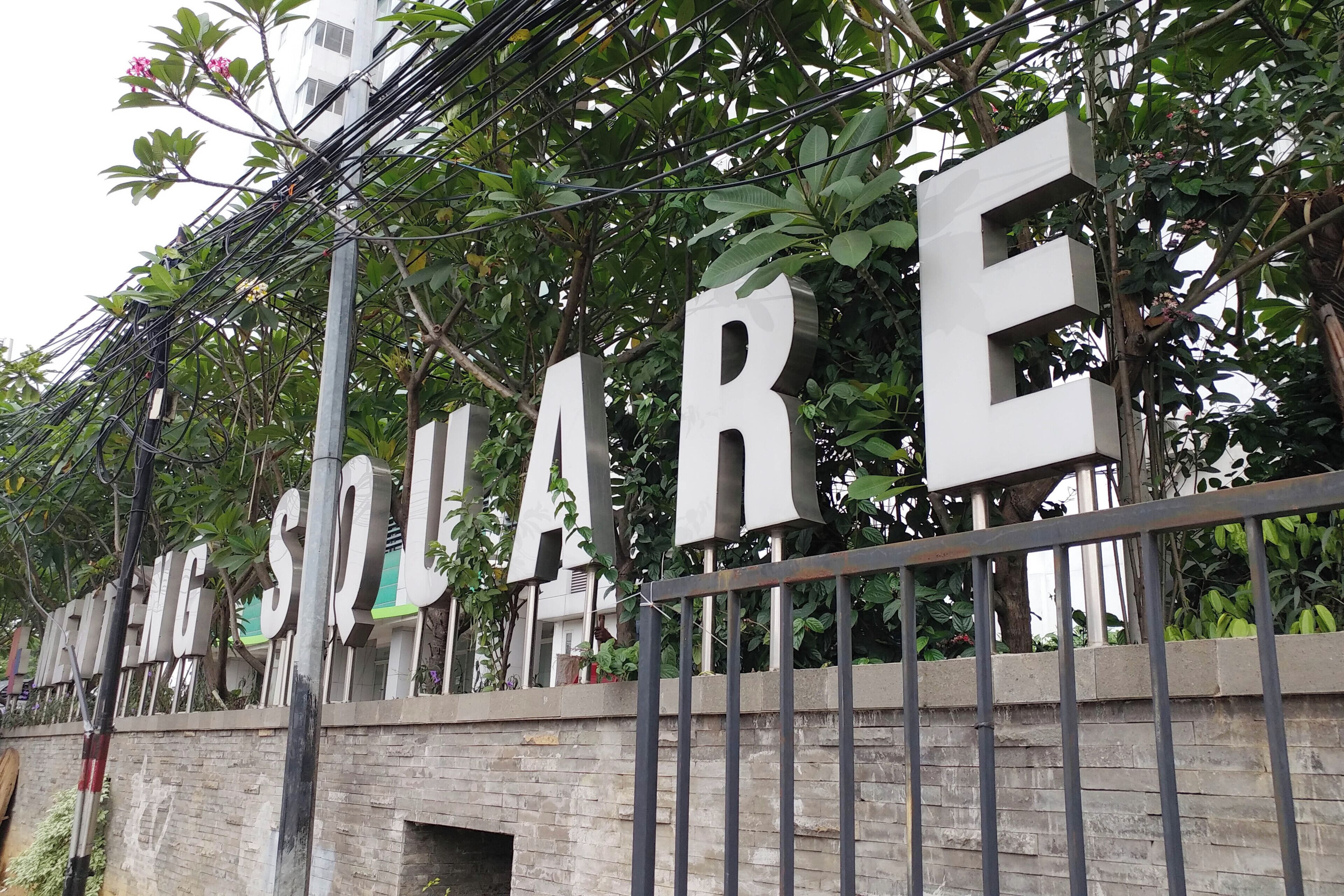 A sign with the word 'SQUARE' in large letters, mounted on a metal fence with greenery in the background.