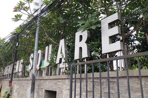 Un letrero con la palabra 'SQUARE' en letras grandes, sujeto a una valla metálica con follaje de fondo.