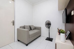 Una sala de estar moderna con un sofá, un ventilador de pie y una mesita con un florero y libros.