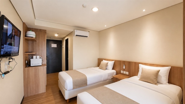 A hotel room with two beds, a TV, a desk with a computer, and an air conditioning unit. - Compact Look Studio (No Kitchen) At Apartment Great Western (Tangerang)