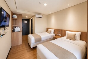 Habitación de hotel con dos camas, un televisor, un escritorio con una computadora y un aire acondicionado.