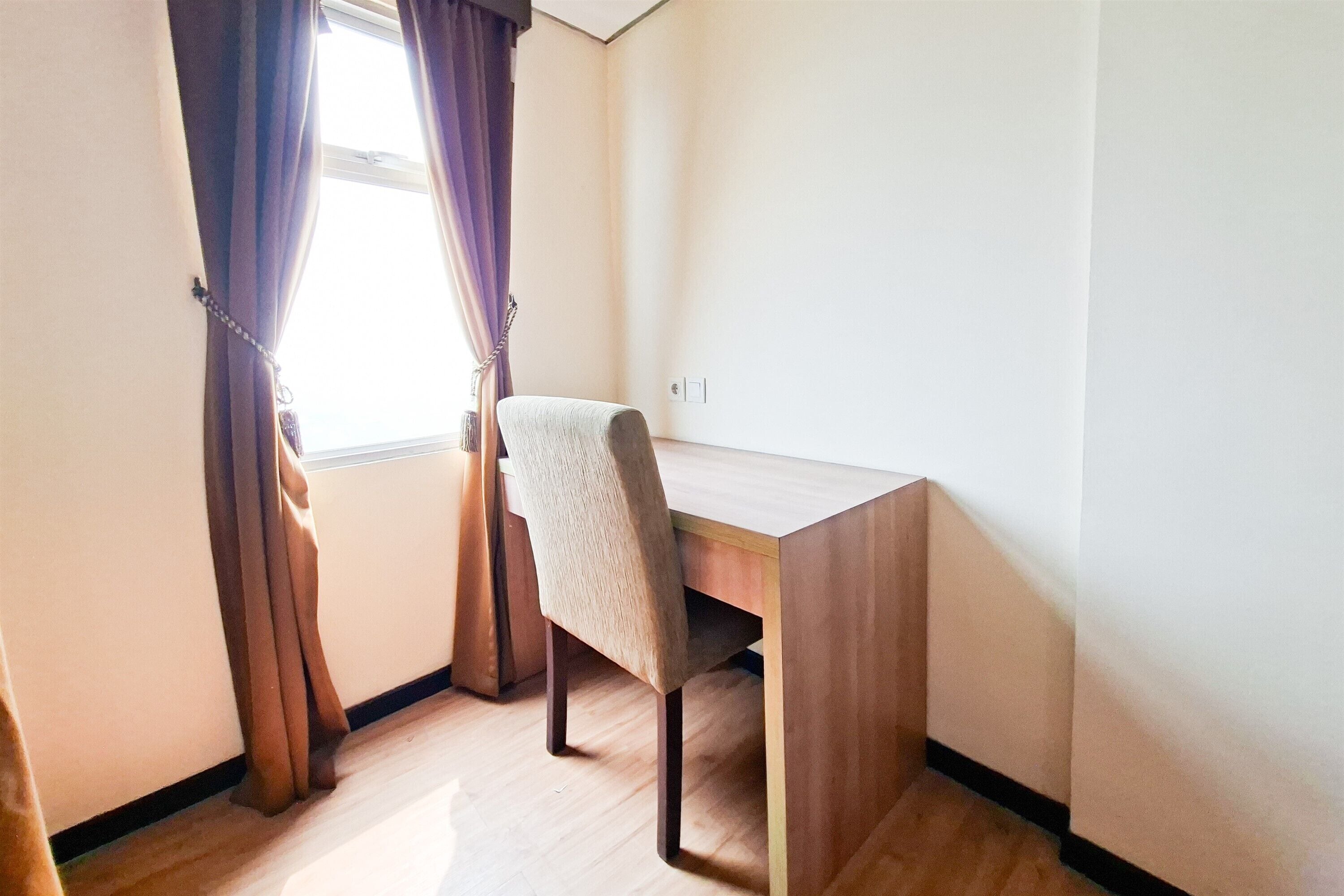 Quarto com escrivaninha de madeira, uma cadeira e janela com cortinas.