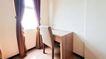 Quarto com escrivaninha de madeira, uma cadeira e janela com cortinas.