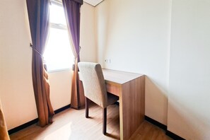 Una habitación con un escritorio de madera, una silla y un ventanal con cortinas.