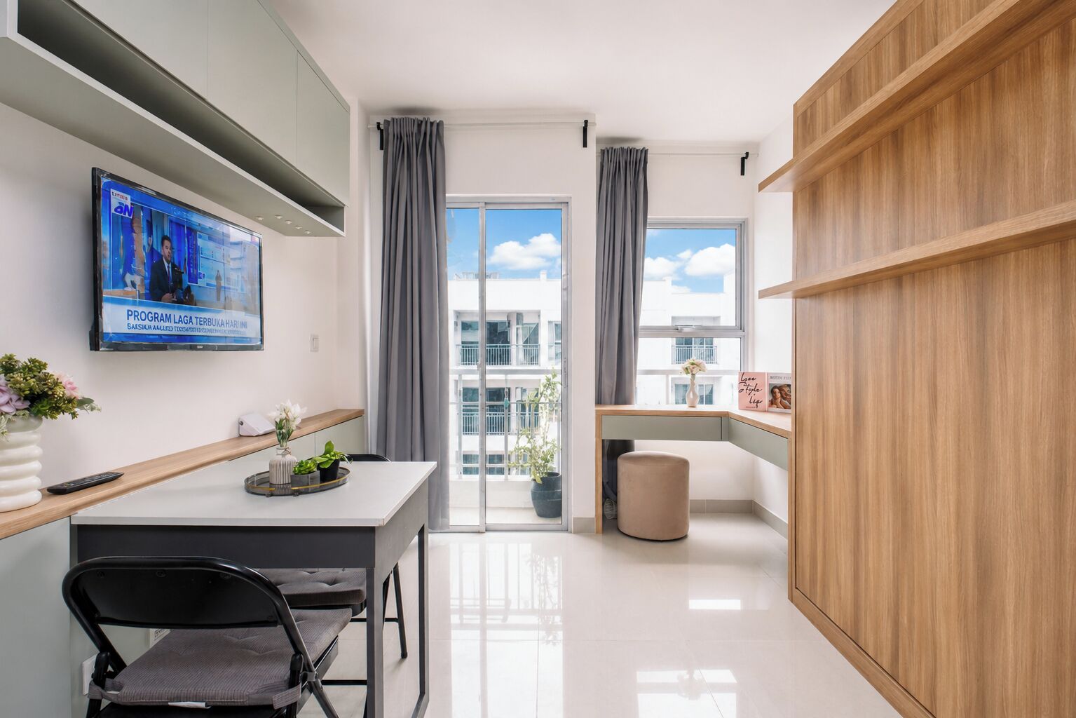 A modern kitchen with a TV, a dining area with a table and chairs, and a view of the outside through large windows.