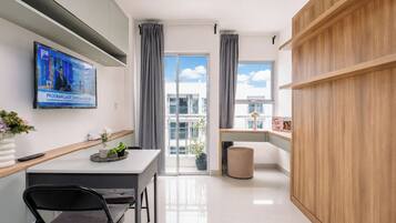 A modern kitchen with a TV, a dining area with a table and chairs, and a view of the outside through large windows.