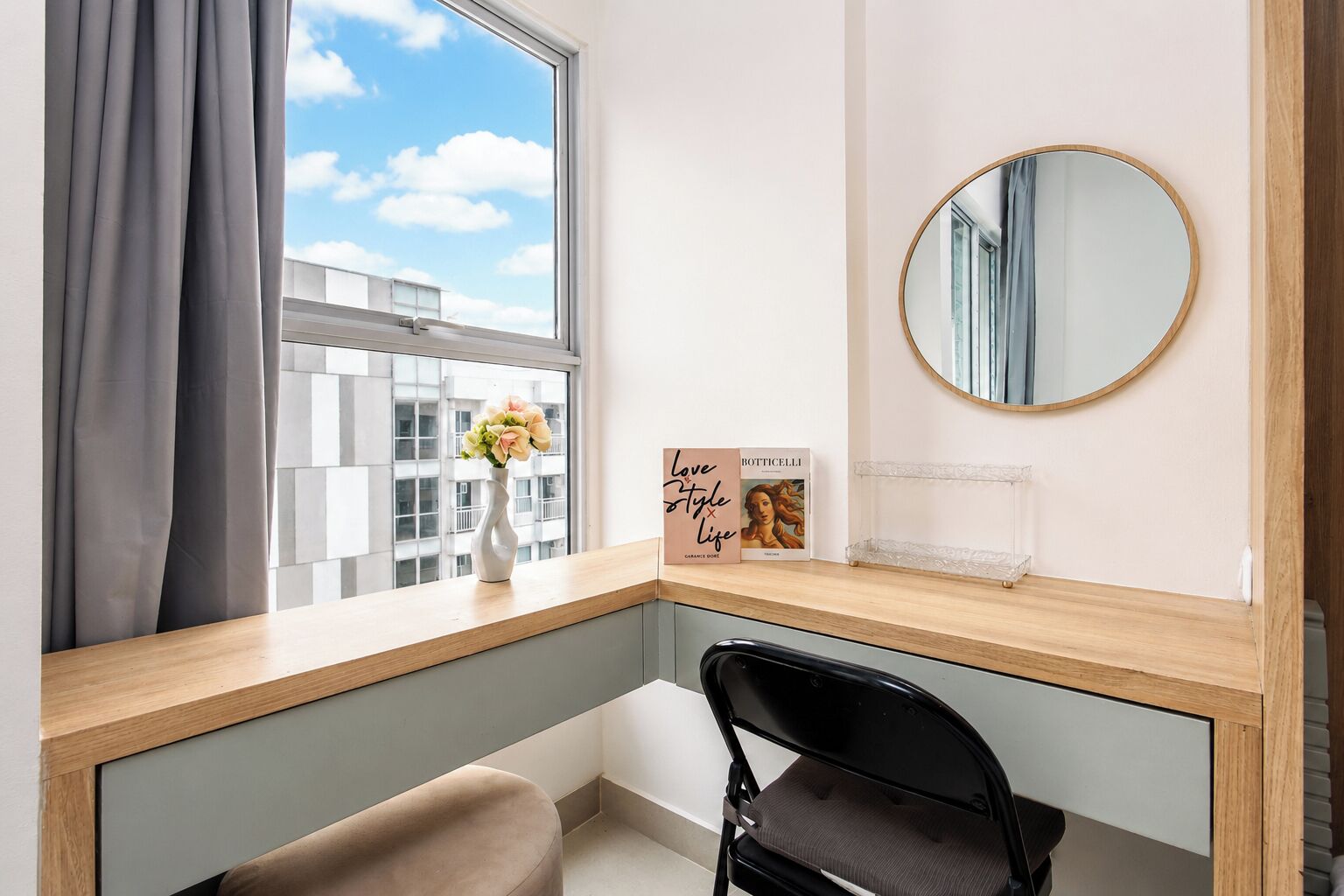 A modern bedroom with a large window, a bedside table, a mirror, and a chair.