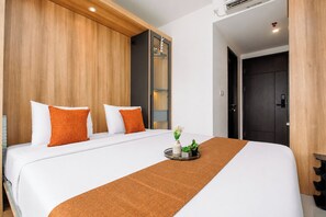 Ein Hotelzimmer mit einem großen Bett, einem Holzkopfteil, weißer Bettwäsche und einem kleinen Tisch mit Tablett und Pflanzen.