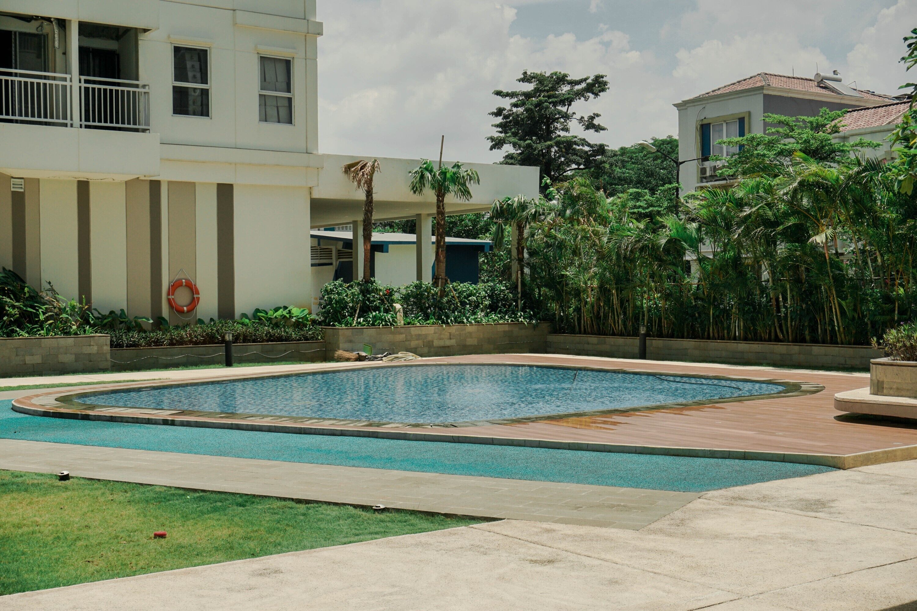 A swimming pool with a surrounding deck, a lifebuoy, and a building with balconies and windows.