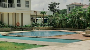 A swimming pool with a surrounding deck, a lifebuoy, and a building with balconies and windows.