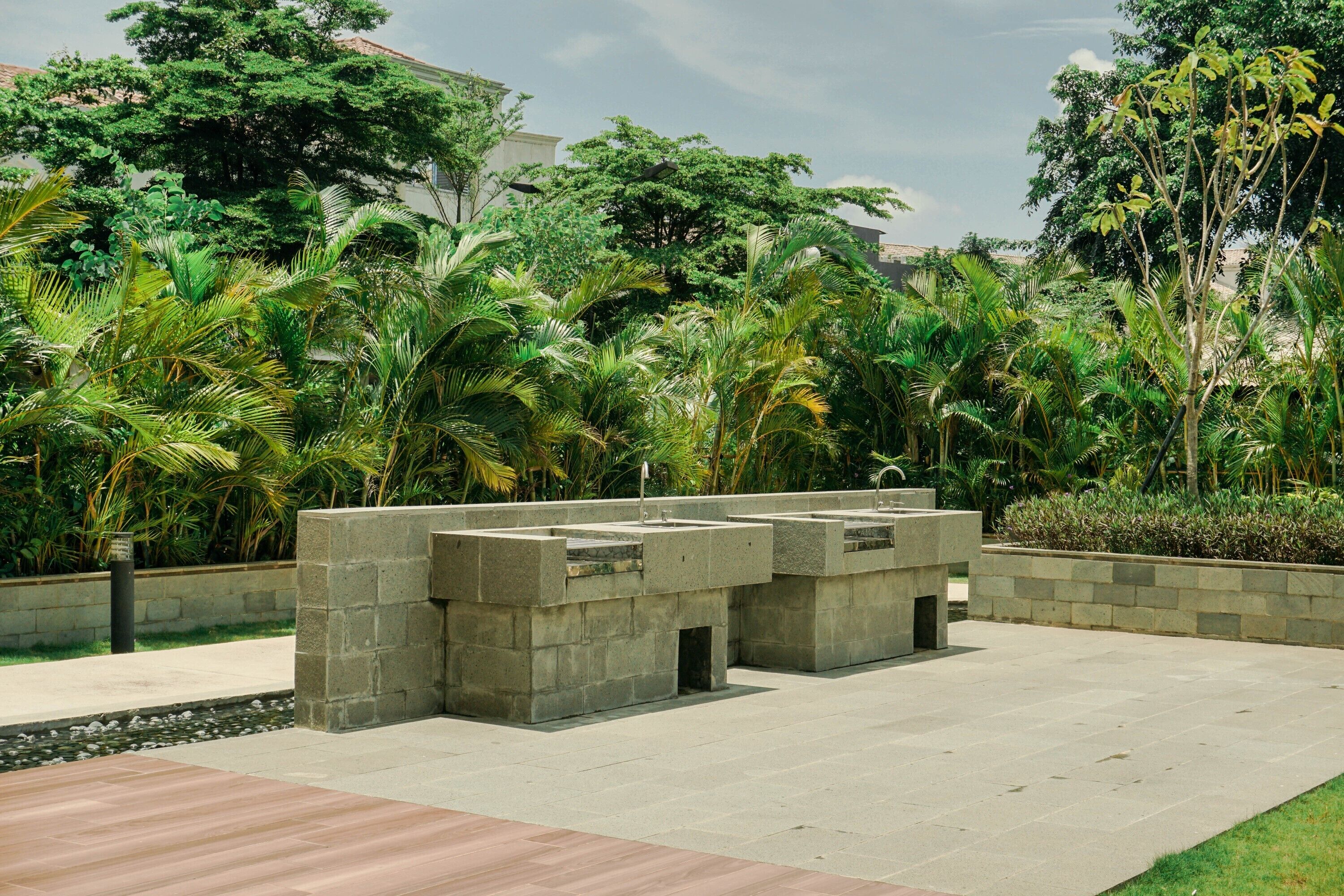 A concrete structure with a water feature, surrounded by lush greenery and a paved walkway.
