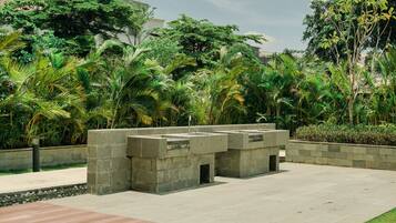 A concrete structure with a water feature, surrounded by lush greenery and a paved walkway.
