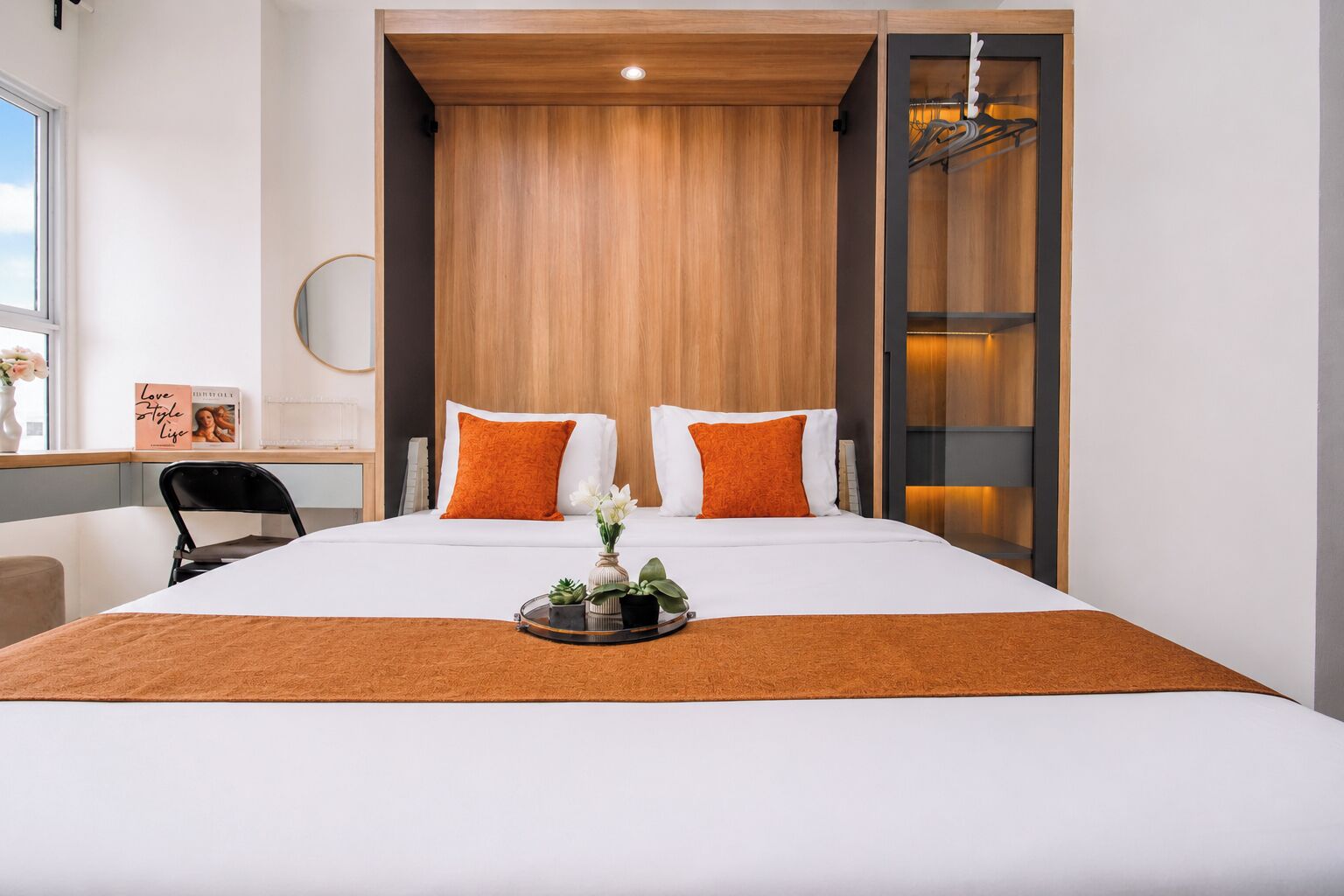 A modern hotel room with a large bed, two pillows, a bedside table, a chair, and a window.