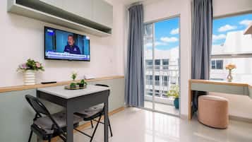 Una sala de estar moderna con un televisor de pantalla plana montado en la pared, un comedor con mesa y sillas, un sofá, y un balcón con vistas a la ciudad.