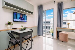 Un saló modern amb un televisor de pantalla plana fixat a la paret, zona de menjador amb taula i cadires, sofà i un balcó amb vista a la ciutat.