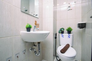 Et badeværelse med en hvid vask, et spejl, et toilet med et håndklæde og to krukker med planter.