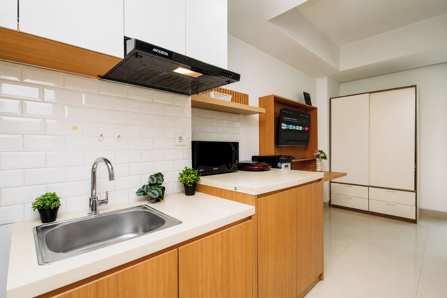 Una cocina moderna con un lavamanos de acero inoxidable, armarios de madera, una campana extractora negra, un microondas y una pequeña planta en maceta.