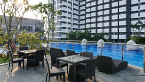 Área de piscina en la azotea con mobiliario exterior y vistas a un edificio alto.